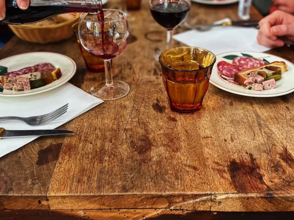 Ambiance conviviale autour d’un déjeuner dans un bouchon lyonnais, charcuterie et vin rouge à table.