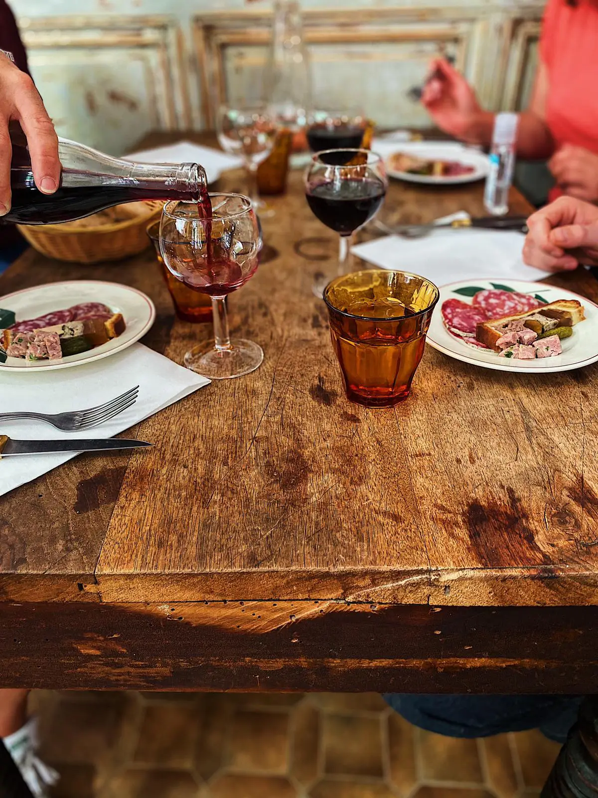 Ambiance conviviale autour d’un déjeuner dans un bouchon lyonnais, charcuterie et vin rouge à table.
